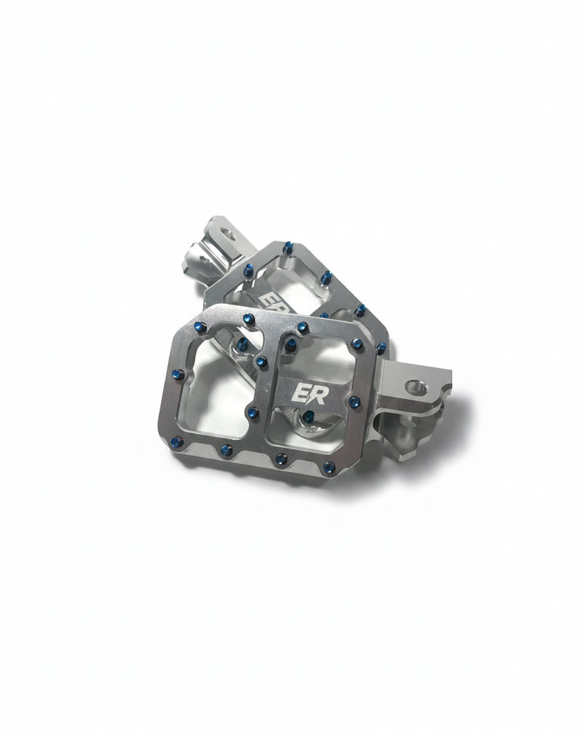 Close-up of ER Moto ETM RTR footpegs stacked, showing ER logo engraving, blue titanium grip screws, and CNC machined open platform design

