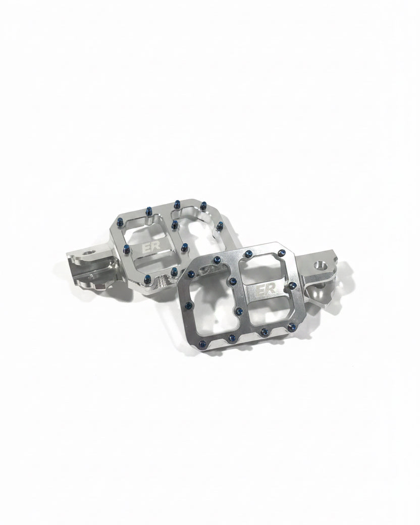 ETM RTR super-wide footpegs pair laid flat showing ER logo, blue grip screws, CNC aluminum construction and mounting brackets

