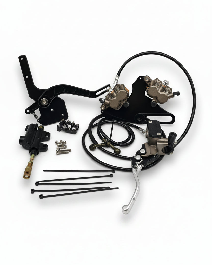 Tuttio footbrake kit black — full kit flat lay with dual caliper mount, two Ultra Bee calipers, footbrake lever, master cylinder, handbrake lever, brake lines, cable ties, and hardware